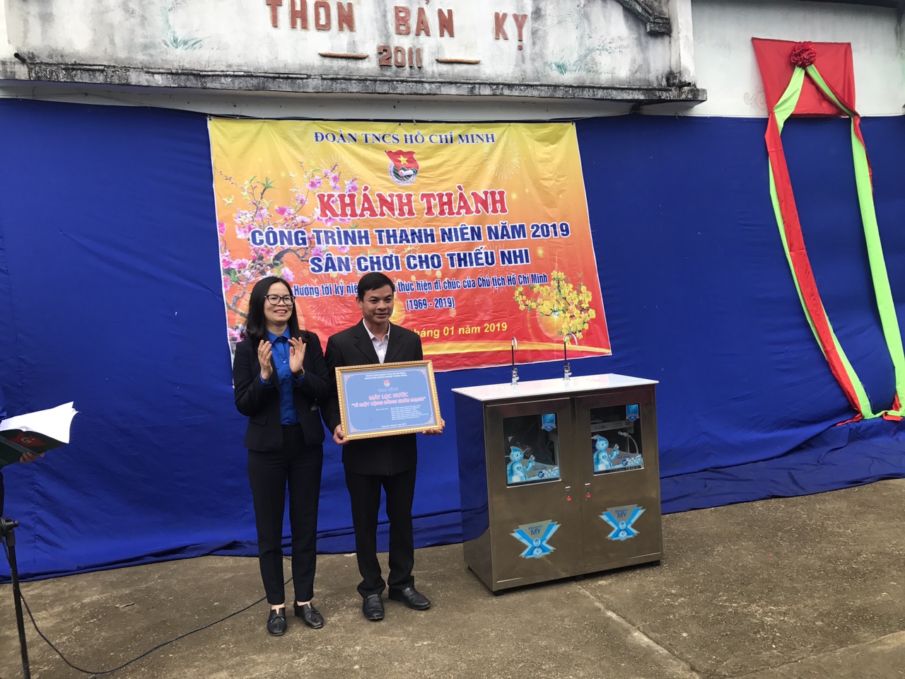 Đồng chí Hoàng Thị Minh Thu, Phó Bí thư Đoàn Khối  trao biển tặng máy lọc nước cho Nhà văn hóa  thôn Bản Kỵ, xã Tri Phương, huyện Tràng Định